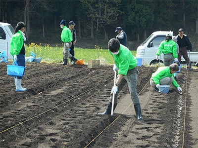 鍬やバケツを持ち畑で作業する人々